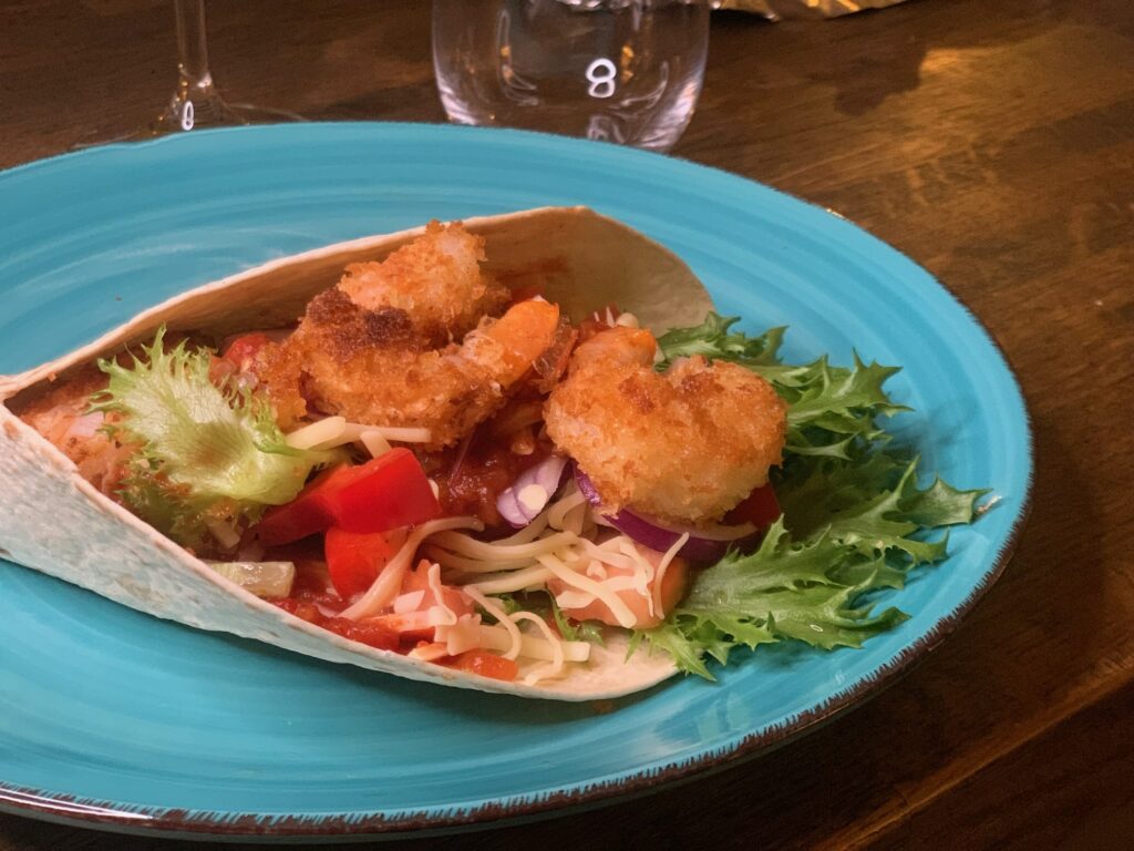 Friterade räkor, med sallad och avokado som ligger i ett tortilla bröd på en grön tallrik.