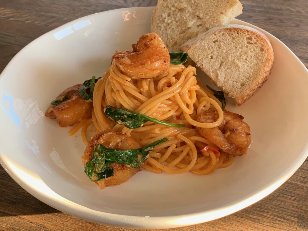 Spaghetti med stora vannameiräkor och spenat och brödskivor i en vit djup tallrik.