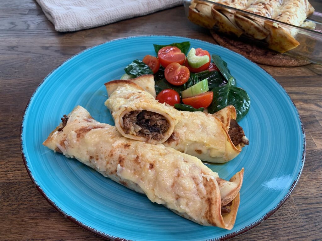 Crepes fyllda med köttfärs och champinjoner med sallad på en grön tallrik.