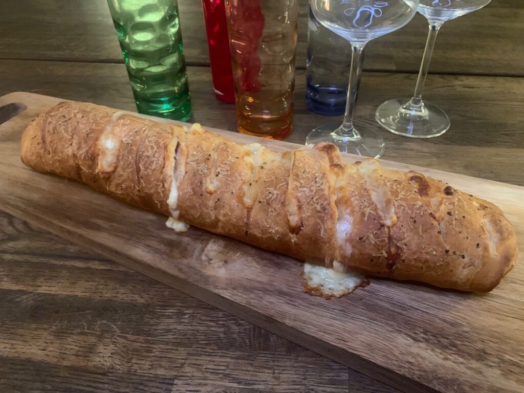 Hel pizza stromboli på träbräda med glas i bakgrunden.