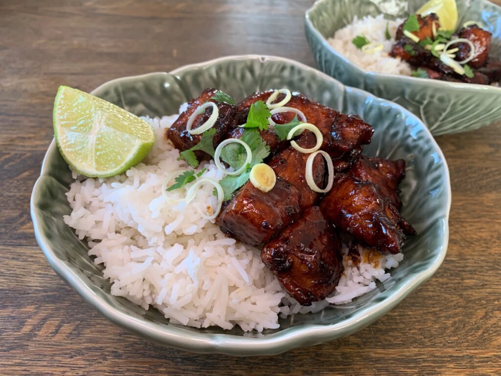 Orange chicken med ris, toppad med koriander och strimlad purjolök och en limeklyfta i en grön djup tallrik.