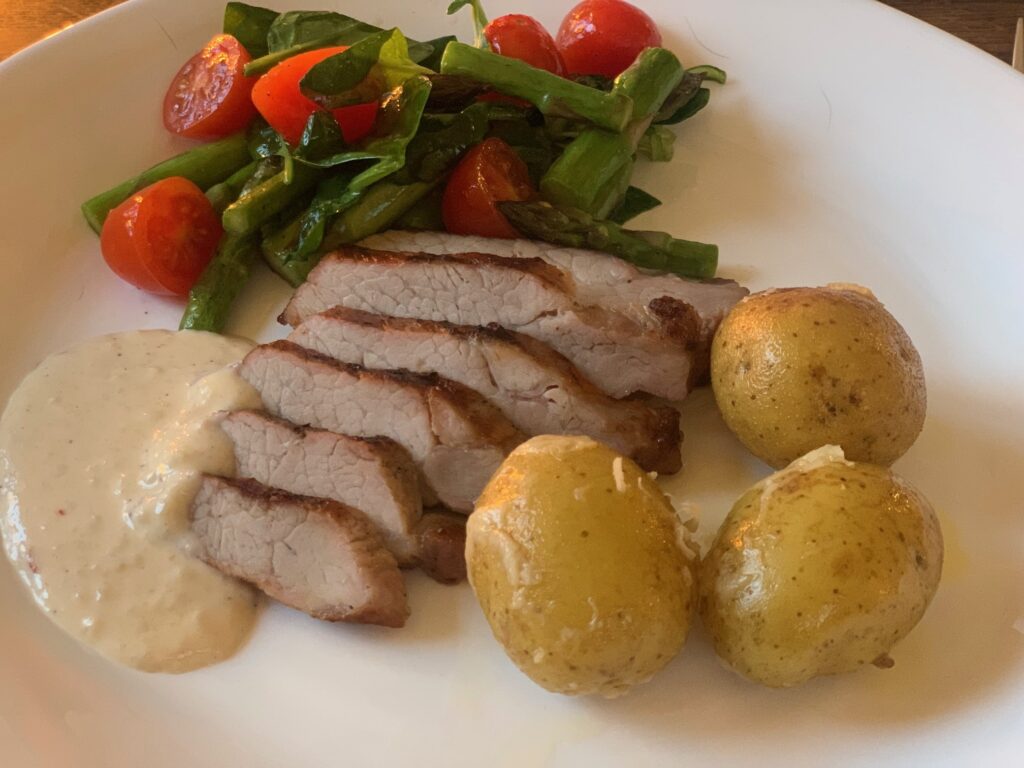 Skivad pluma med potatis, chevresås och sallad på vit tallrik.